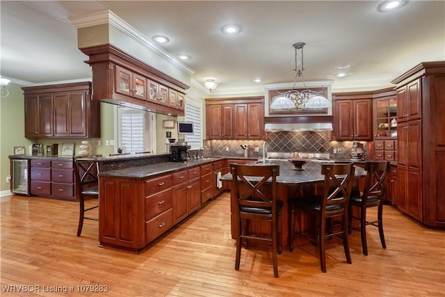 kitchen featuring beverage cooler, a center island with sink, light wood-style flooring, a breakfast bar area, and a sink