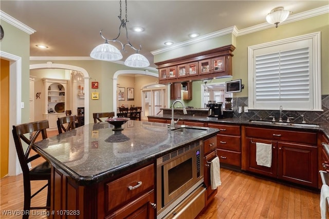 kitchen featuring light wood-style floors, arched walkways, stainless steel microwave, and a sink