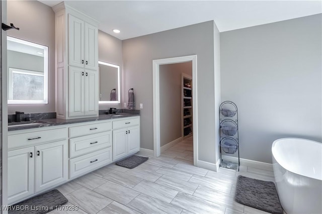 bathroom with a freestanding tub, a sink, baseboards, double vanity, and a walk in closet