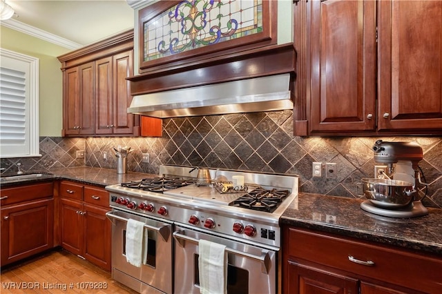 kitchen featuring tasteful backsplash, ornamental molding, wall chimney range hood, dark stone countertops, and double oven range