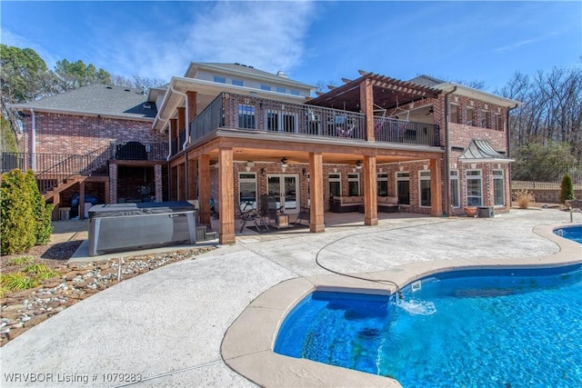 rear view of house featuring brick siding, a patio, a hot tub, and a balcony