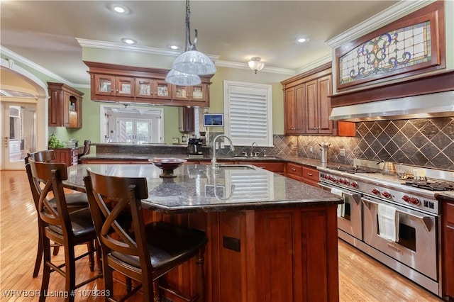 kitchen featuring range with two ovens, a breakfast bar area, a sink, wall chimney range hood, and decorative backsplash