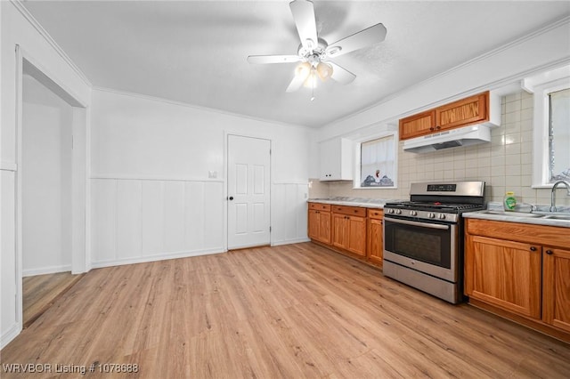 kitchen featuring sink, stainless steel gas range oven, light wood-type flooring, ornamental molding, and decorative backsplash