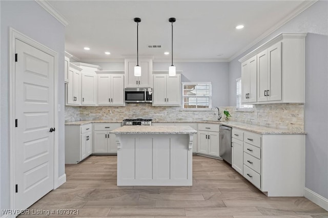 kitchen with appliances with stainless steel finishes, crown molding, pendant lighting, white cabinets, and a kitchen island