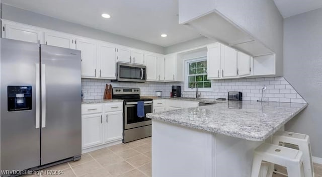 kitchen with kitchen peninsula, white cabinetry, a breakfast bar, and appliances with stainless steel finishes