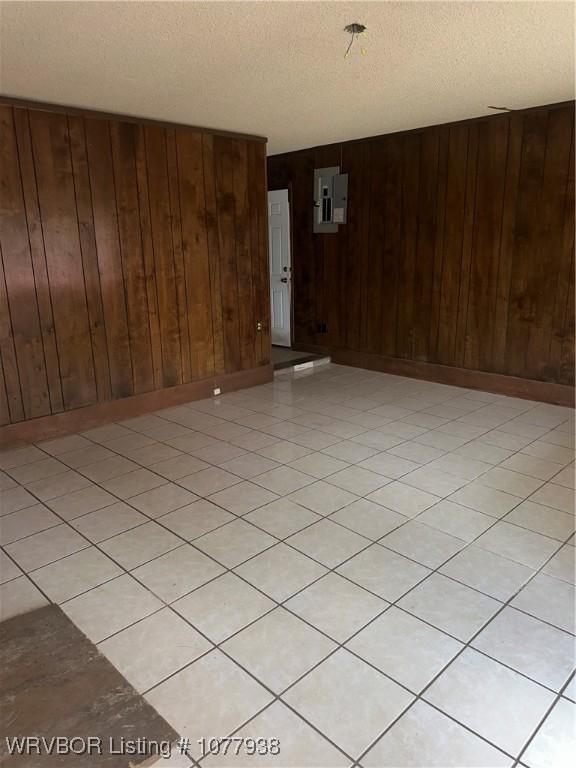 interior space with electric panel, a textured ceiling, and wooden walls