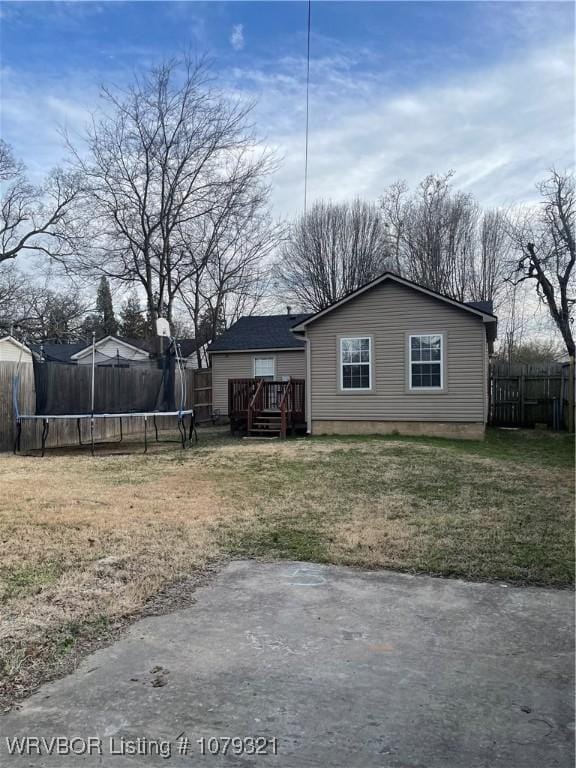 exterior space featuring a deck, a yard, a trampoline, and fence