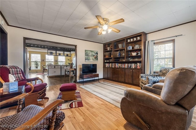 living room featuring built in shelves, hardwood / wood-style flooring, ceiling fan, and ornamental molding