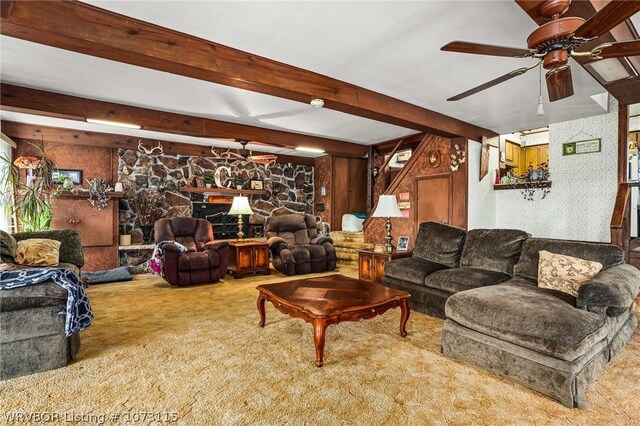 living room featuring carpet flooring, ceiling fan, beam ceiling, and a stone fireplace