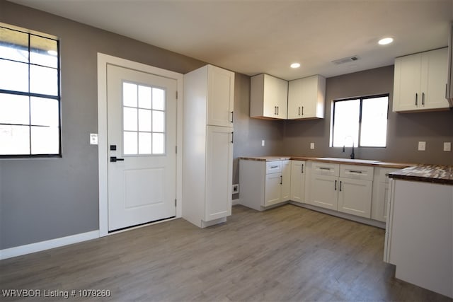 kitchen featuring light wood-type flooring, white cabinets, a sink, and baseboards