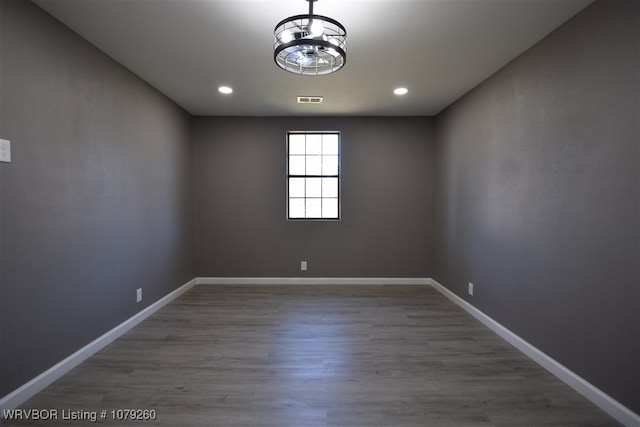 empty room with baseboards, visible vents, wood finished floors, an inviting chandelier, and recessed lighting