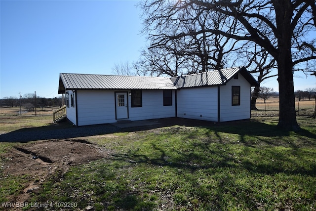 rear view of house featuring entry steps, metal roof, and a lawn