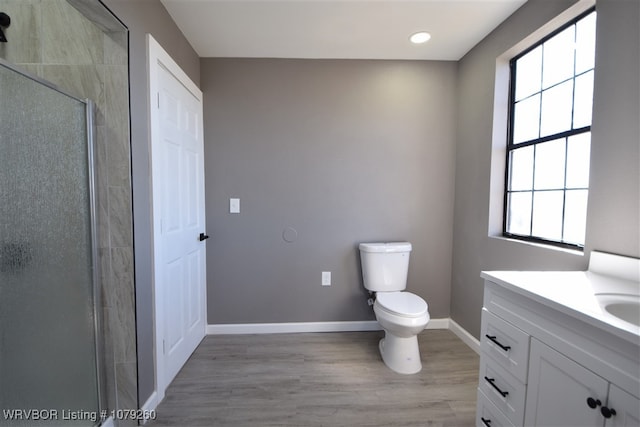 bathroom with toilet, a shower stall, vanity, wood finished floors, and baseboards