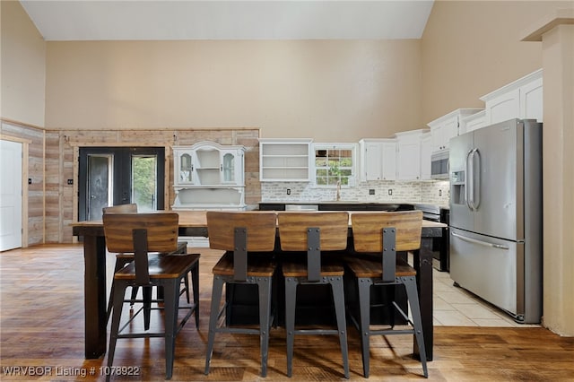 kitchen featuring white cabinetry, backsplash, high vaulted ceiling, stainless steel appliances, and a center island