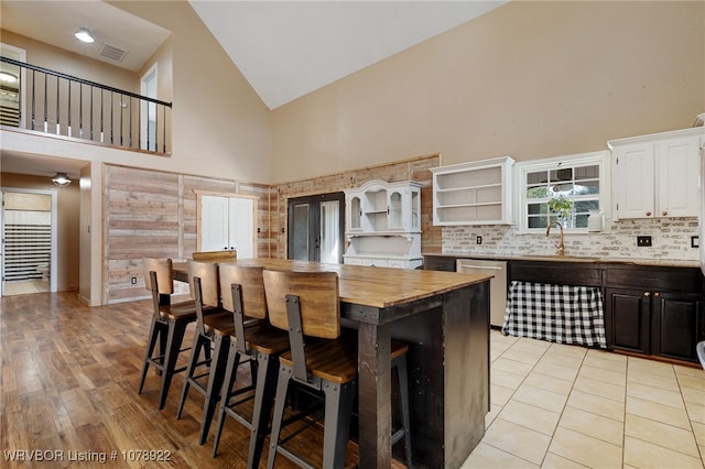 kitchen with high vaulted ceiling, white cabinetry, butcher block counters, a kitchen bar, and a center island