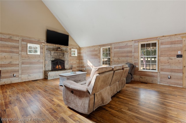 living room featuring a fireplace, wood-type flooring, high vaulted ceiling, and wood walls