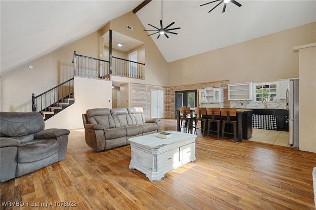 living room with high vaulted ceiling, beamed ceiling, sink, ceiling fan, and light hardwood / wood-style floors