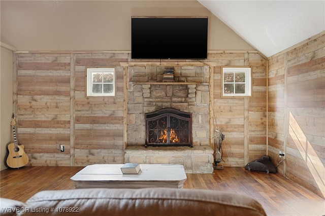 unfurnished living room featuring hardwood / wood-style flooring, vaulted ceiling, a stone fireplace, and wooden walls