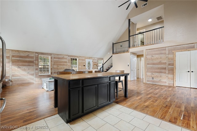 kitchen with a breakfast bar, wood walls, a center island, high vaulted ceiling, and light hardwood / wood-style floors