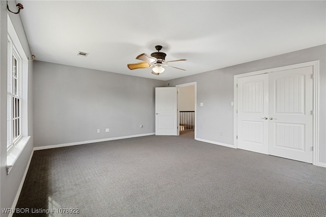 unfurnished bedroom with multiple windows, a closet, ceiling fan, and dark colored carpet