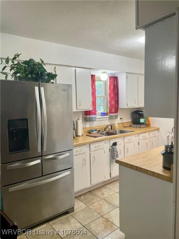 kitchen featuring sink, white cabinets, light tile patterned floors, stainless steel fridge with ice dispenser, and a textured ceiling