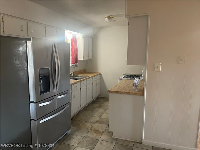 kitchen featuring stove, light tile patterned flooring, sink, white cabinetry, and stainless steel fridge with ice dispenser