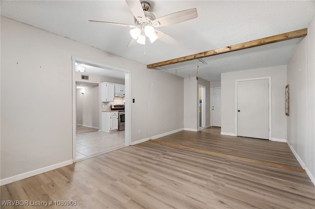 unfurnished living room featuring a ceiling fan, light wood-style floors, baseboards, and attic access