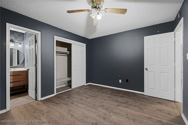 unfurnished bedroom featuring wood finished floors, a textured ceiling, baseboards, and connected bathroom