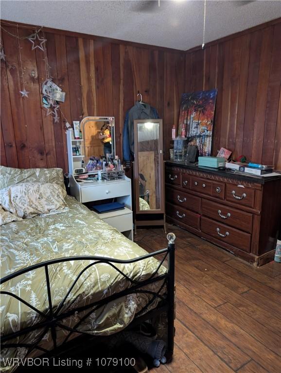 bedroom with wooden walls, a textured ceiling, and wood finished floors