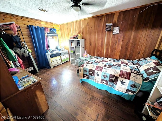 bedroom featuring visible vents, wooden walls, hardwood / wood-style floors, and a textured ceiling