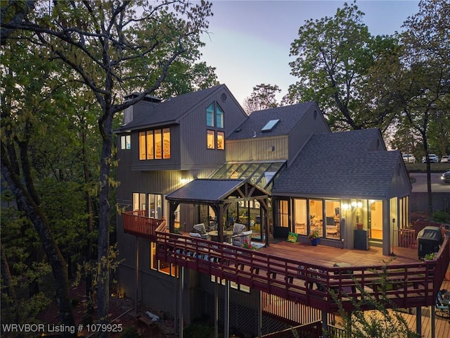 back of house at dusk with roof with shingles and a deck
