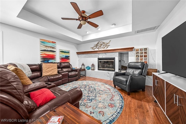 living room featuring visible vents, a raised ceiling, a ceiling fan, a high end fireplace, and wood finished floors