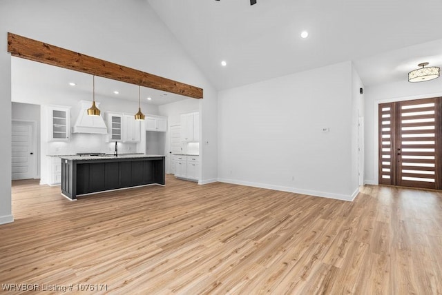 kitchen with pendant lighting, custom exhaust hood, white cabinets, an island with sink, and light hardwood / wood-style floors