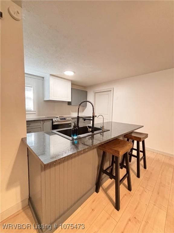 kitchen with white cabinetry, sink, a kitchen breakfast bar, kitchen peninsula, and light hardwood / wood-style floors