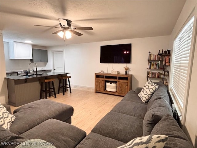 living room featuring a textured ceiling, light hardwood / wood-style flooring, ceiling fan, and sink