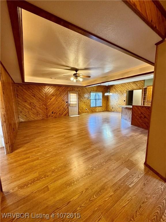 unfurnished living room with ceiling fan, wood walls, beam ceiling, and light hardwood / wood-style flooring