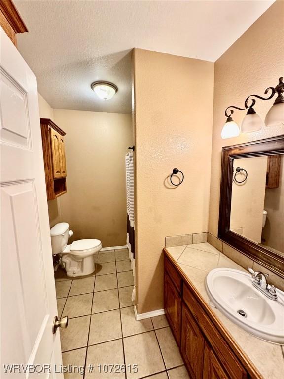 bathroom featuring vanity, a textured ceiling, tile patterned floors, and toilet