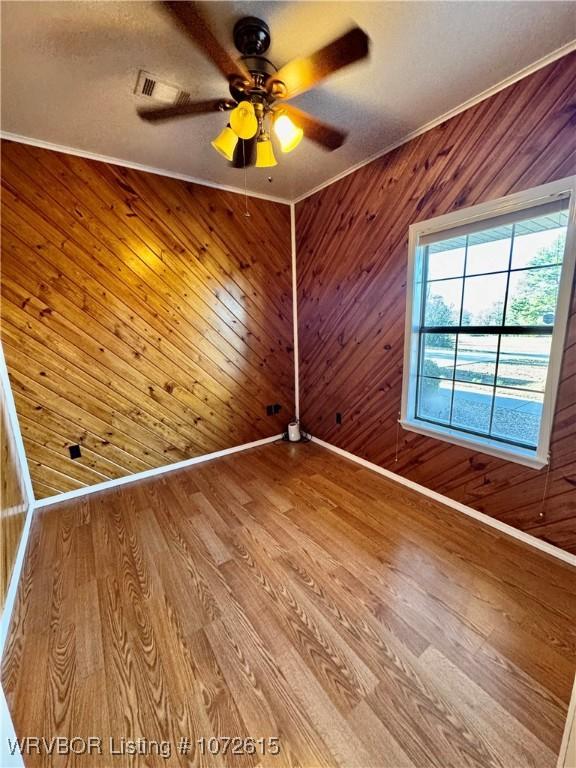 unfurnished room with ceiling fan, light wood-type flooring, crown molding, and wooden walls