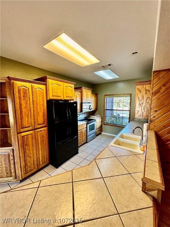 kitchen featuring black fridge, sink, light tile patterned floors, electric range, and tile counters