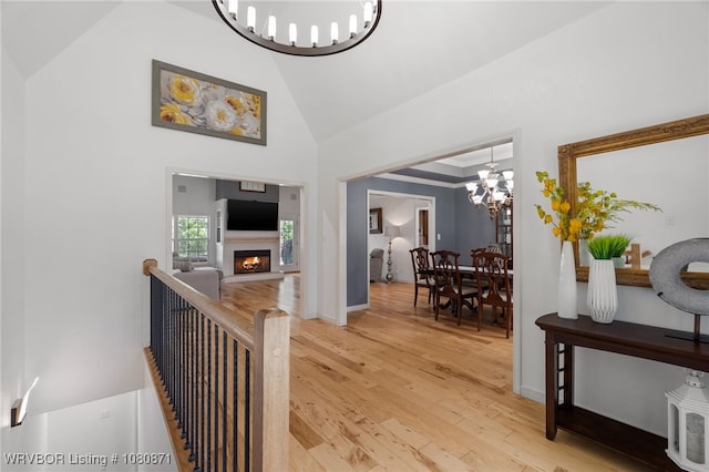 hall with a chandelier, light wood finished floors, high vaulted ceiling, and baseboards