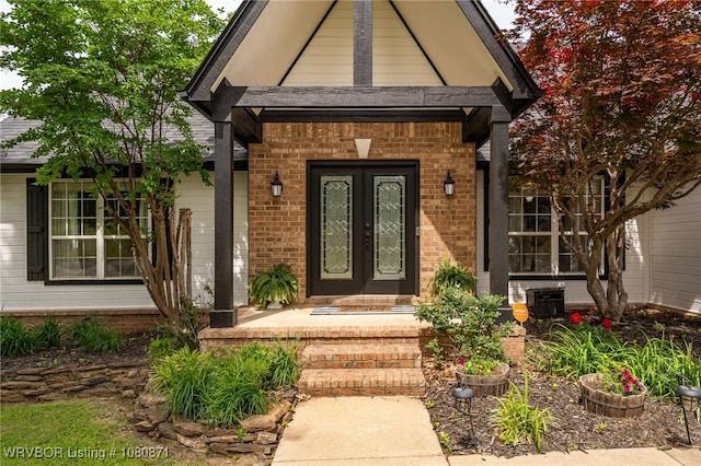 view of exterior entry featuring french doors, brick siding, covered porch, and central air condition unit