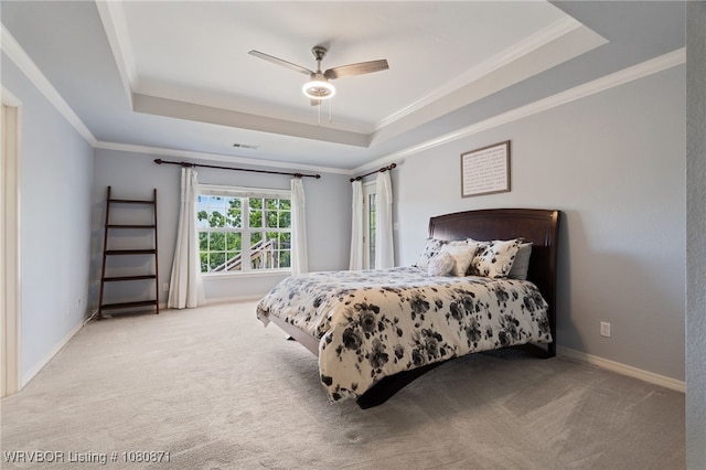 carpeted bedroom featuring a tray ceiling, ornamental molding, ceiling fan, and baseboards