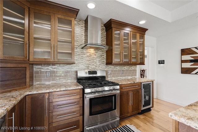 kitchen with gas stove, wall chimney range hood, beverage cooler, light wood-style floors, and backsplash