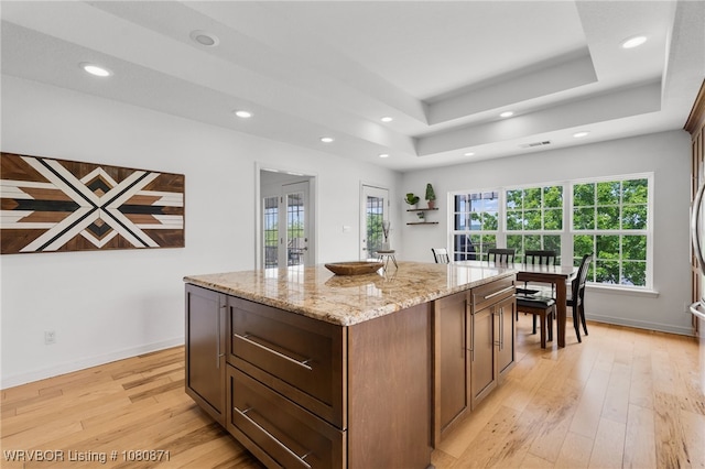 kitchen with light wood-type flooring, a tray ceiling, a kitchen island, recessed lighting, and light stone counters