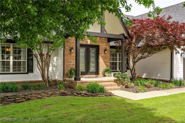 entrance to property with french doors, a yard, and brick siding