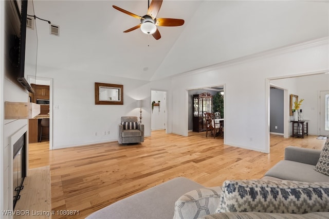 living area with ceiling fan, high vaulted ceiling, light wood finished floors, a glass covered fireplace, and baseboards