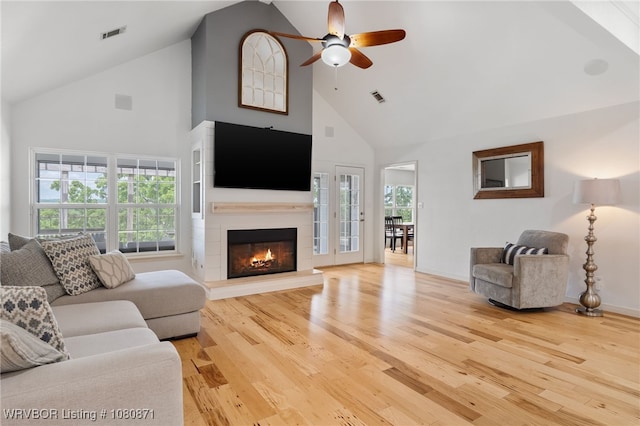living area with high vaulted ceiling, a ceiling fan, wood finished floors, and a glass covered fireplace
