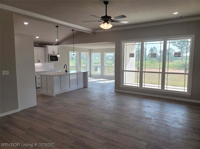 kitchen featuring pendant lighting, built in microwave, white cabinets, a kitchen island with sink, and decorative backsplash