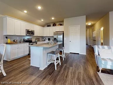 8011 Windflower Ln, Fort Smith, AR 72916 - kitchen with appliances with stainless steel finishes, a breakfast bar area, white cabinets, dark wood-style flooring, and lofted ceiling
