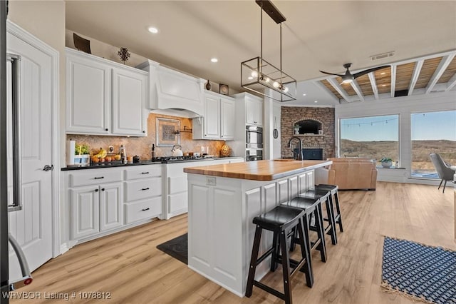 kitchen with light hardwood / wood-style flooring, white cabinetry, a kitchen island with sink, wood counters, and decorative light fixtures